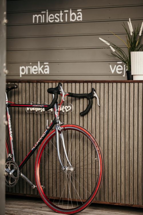 Sarkans velosipēds pie koka sienas ar uzrakstiem.
