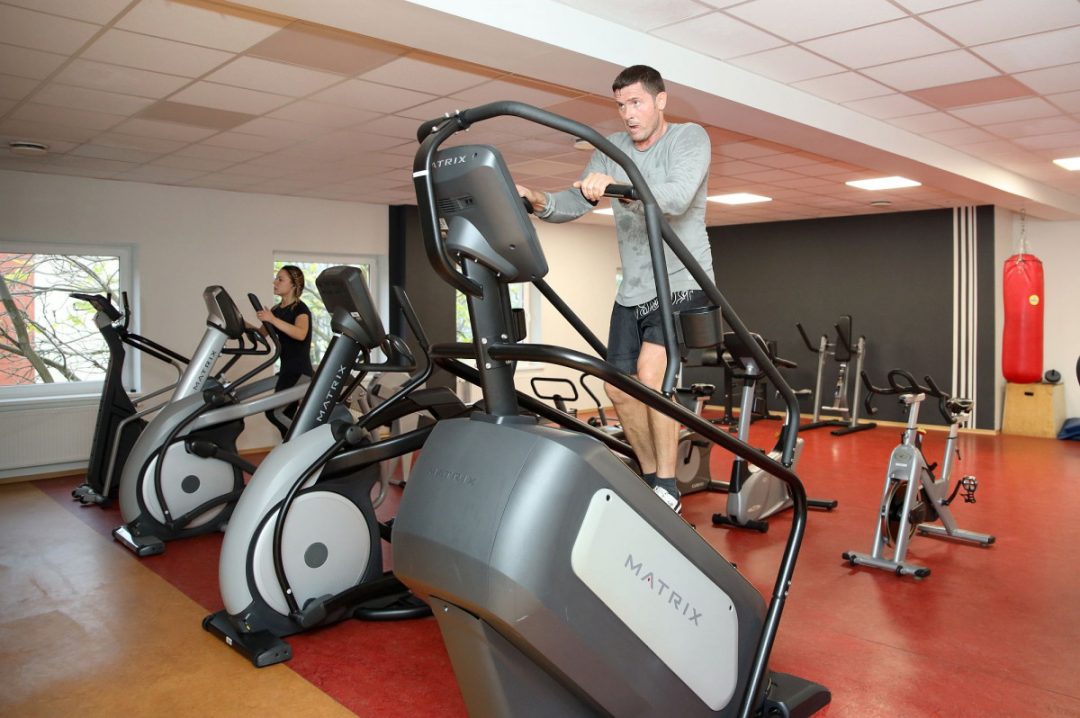 Vīrietis un sieviete trenējas sporta zālē uz trenažieriem.