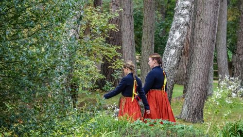 Divas sievietes tradicionālās drēbēs mežā.