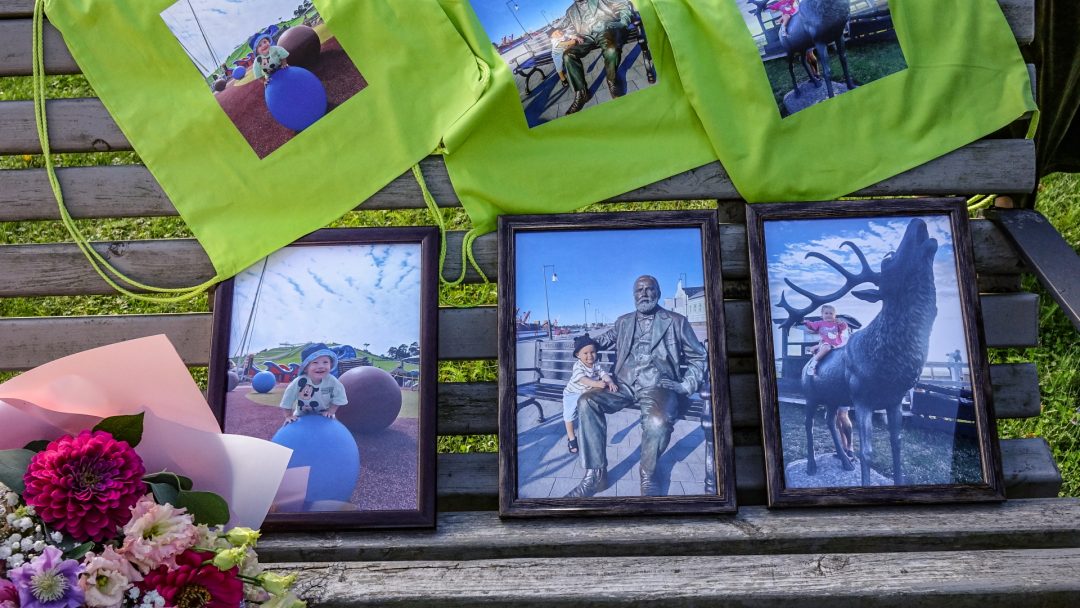 Zaļi maisiņi un bērnu fotogrāfijas uz soliņa ar ziediem.