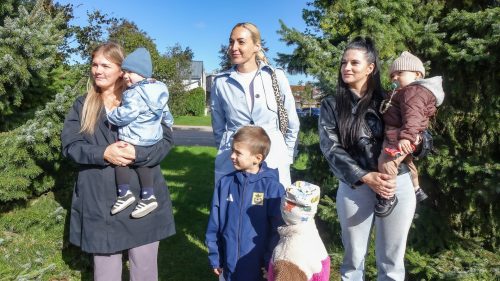 Cilvēki parkā saulainā dienā, bērni un pieaugušie kopā.