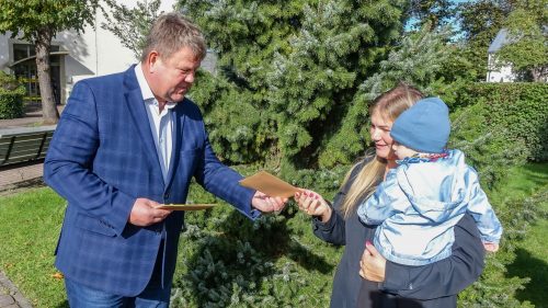 Vīrietis dāvina aploksni sievietei ar bērnu parkā.